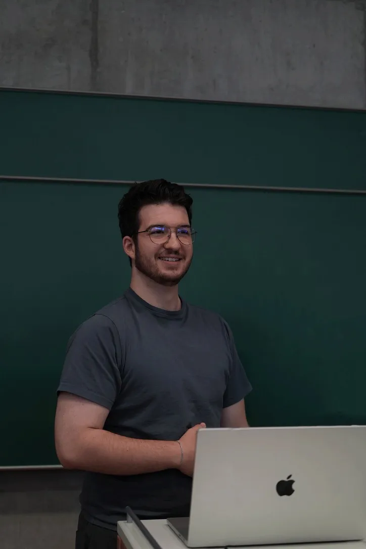 Fabian Bitzer standing at a lectern with a laptop in a lecture hall, smiling.